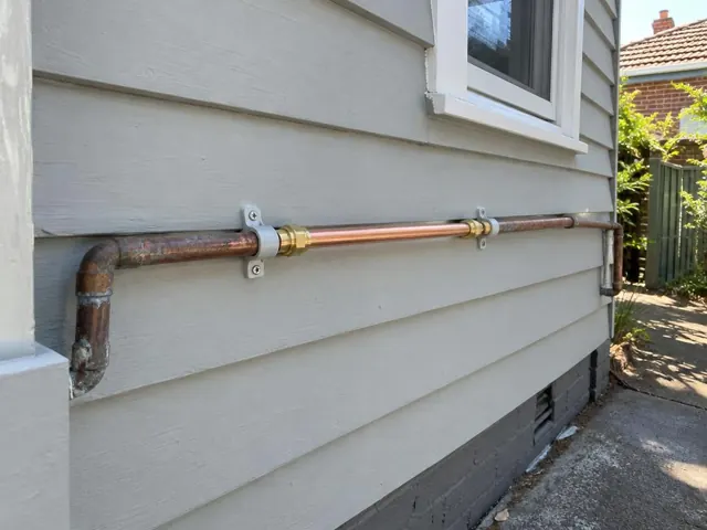 Repaired copper water pipe on an exterior weatherboard wall beside a window in Kingsford