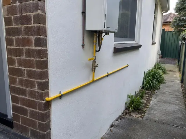 Yellow gas pipe and fittings on an exterior brick and rendered wall beside a window in Kingsford